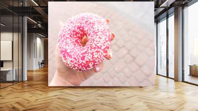 Pink doughnut in a girl's hand with copy space. donut with a pink chocolate frosting. Sweet dessert festive. Breakfast and bachelorette party concept. Wall mural