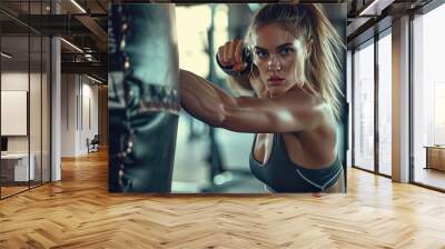 mujer joven deportista boxeadora golpeando un saco de boxeo, vistiendo ropa deportiva, sobre fondo de gimnasio desenfocado Wall mural