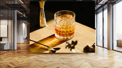 whisky drink on a wooden table with a barspoon and a jigger on black background Wall mural