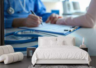 A stethoscope lays on a desk with a doctor consulting a patient in the background. Wall mural