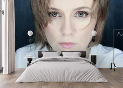 Closeup portrait of a young woman with green eyes and blond hair on a dark blue background. Very serious, attentive look. Ring light is reflected in the eyes. Wall mural