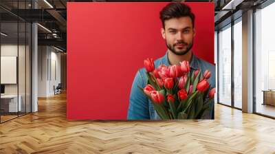 Portrait of a handsome young man standing isolated over red background, holding tulips bouquet Wall mural