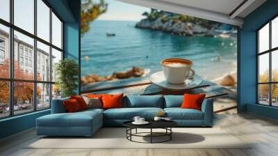 Cup of coffee with beautiful latte art on a wooden terrace table with a stunning view of a turquoise sea and rocky coastline. Relaxation on a summer holiday vacation by the sea. Wall mural