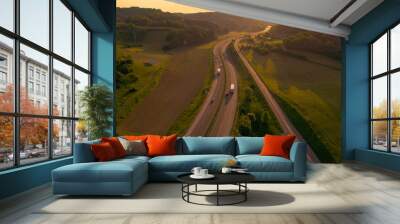 AERIAL, LENS FLARE: Smooth running traffic on a motorway winding through hills and lush green countryside. Cars and trucks travel along the highway as morning light illuminates picturesque landscape. Wall mural