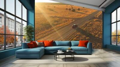 AERIAL: Black SUV car driving along empty country road at golden summer sunset Wall mural