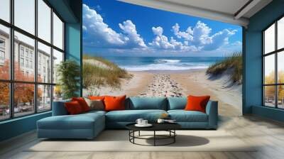 A path leads to the beach through a sand dune with clear blue sky and white clouds. Wall mural