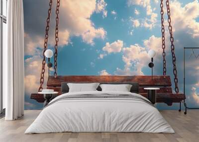 A rustic wooden swing hangs against a bright blue sky with fluffy white clouds. Wall mural