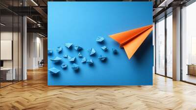 A single orange paper airplane leading a group of blue paper airplanes on a blue background. Wall mural