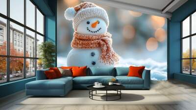 A snowman with a knitted hat and scarf stands in the snow with a bokeh background. Wall mural