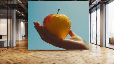 Hand holding a red and yellow apple covered in honey against a blue sky. Wall mural