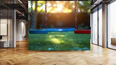 Two empty swings hanging in a green backyard with a blue and red seat, the sun shining through the trees. Wall mural