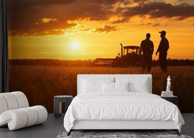 Two farmers stand in a field at sunset, silhouetted against the glowing sky with a tractor in the background. Wall mural