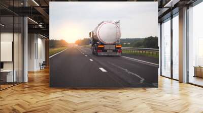 A truck with a semi-trailer transports a dangerous chemical cargo in a tank car on a highway against the background of a sunset. Sanctions in cargo transportation Wall mural