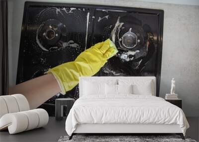 The hands of a girl in yellow gloves apply an anti-grease product to a gas stove with soot and dirt. Cleaning company services for cleaning kitchen appliances. Copy space for text Wall mural