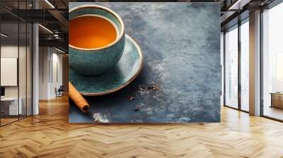 Steaming cup of aromatic spiced tea with a cinnamon stick placed on a rustic wooden table setting  The warm and cozy beverage evokes a sense of comfort and relaxation Wall mural