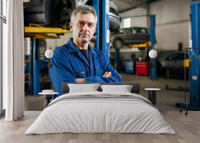 A mechanic in a blue jumpsuit stands with arms crossed in an automotive repair shop. Car lifts and vehicles are visible in the background. Wall mural