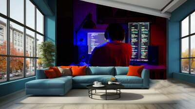 A man sits at a computer in a room at a table at night with blue lighting and programs Wall mural