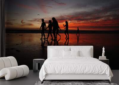 Friends walk across the beach at sunset. Wall mural