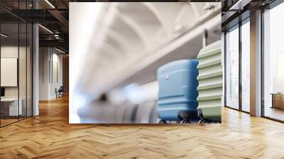 A close-up of two suitcases on the overhead storage rack in an airplane, one green and another blue Wall mural