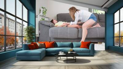 Loving mother tickling her little daughter on the sofa at home. High quality photography Wall mural