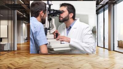 male doctor ophthalmologist is checking the eye vision of handsome young man in modern clinic. Doctor and patient in ophthalmology clinic . Wall mural