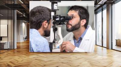 male doctor ophthalmologist is checking the eye vision of handsome young man in modern clinic. Doctor and patient in ophthalmology clinic . Wall mural