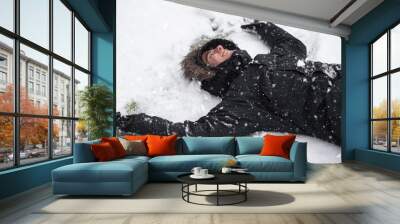 Young man laughing, with happy expression, snow covered, lying on the ground in snowfall .  Wall mural