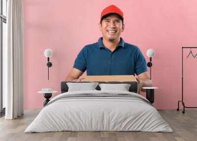 Happy young delivery man in red cap standing with parcel post box Wall mural