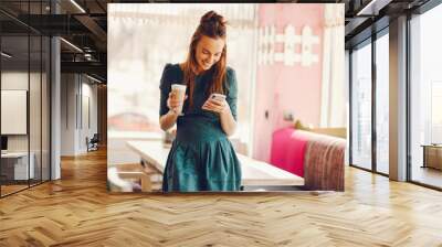 beautiful and stylish woman with long hair and in a green dress standing in a cafe at the table and drinking coffee and using the phone Wall mural