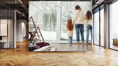 Beautiful mother with children. Family at home. People standing near winter windows Wall mural