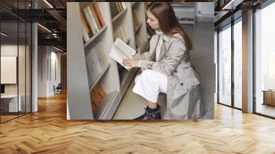 Girl in the library. Student looking for a book. Lady in a brown coat. Wall mural