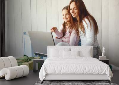 Little girl looking at laptop with her mother. Woman in a white sweater. Enjoying spending time together. Wall mural