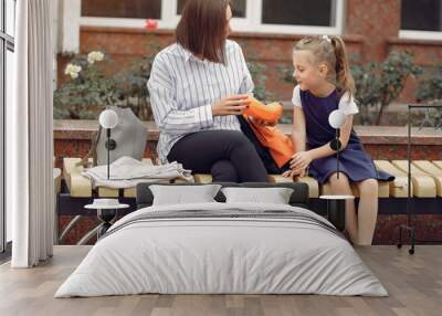 Mother and daughter. Mom puts in the backpack of baby stuff. Family sitting on a bench. Wall mural