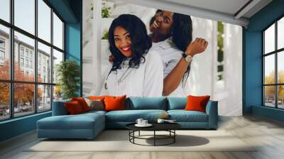 Stylish black doctor in a white uniform. Ladies with stethoscope. Two girls in a white robes Wall mural