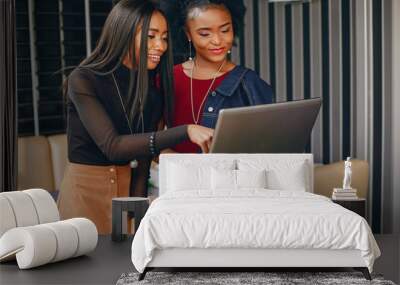 two beautiful and stylish young, dark girls standing in a restaurant and using a laptop Wall mural