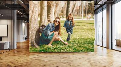 young and stylish mother with long hair and a jeans jacket playing with her little cute daughter in the summer park Wall mural