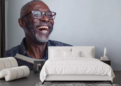 A middle-aged black man wearing glasses is reading a book while laughing, isolated on white background Wall mural