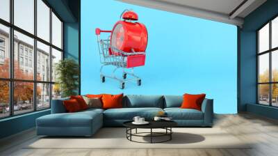 Shopping cart and classic alarm clock on blue background. Sale time buy mall market shop consumer concept. Selective focus. Wall mural