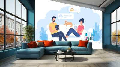 Young couple sitting on a white sofa with their funny cat and reading some information in internet Wall mural