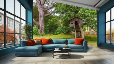 Cozy little wooden playhouse in an old big tree in a public park with stairs and windows, Wall mural