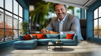 A joyful middle-aged businessman in a grey suit, seated at an office desk. Wall mural