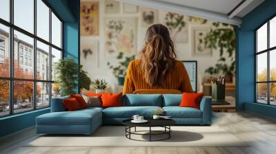 A young woman sits at a desk in her home office, facing away from a laptop on the table. Wall mural