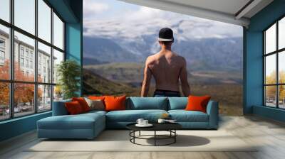 Backside of tall muscular caucasian man with naked torso standing in over mountain and sky background. Promoting active, sport and healthy lifestyle Wall mural