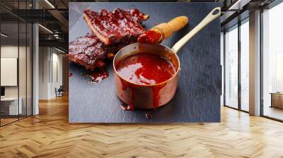 Hot and spicy barbecue sauce in a casserole as close-up with spare ribs in background Wall mural