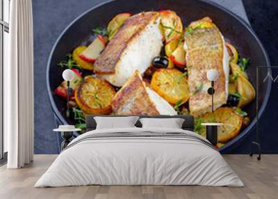 Modern style traditional fried skrei cod fish filet with fried potato, fruits and olives served as close-up in a design cast iron pan Wall mural