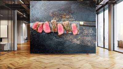 Traditional barbecue aged venison backstrap roast sliced with herbs as top view on a large knife with rustic background with copy space Wall mural