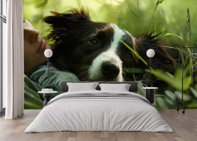 A border collie with a black and white coat lounges beside its owner in a lush green meadow in a relaxing moment creating a charming copy space image Wall mural