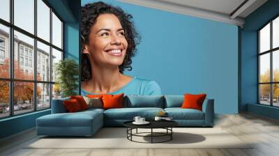 A Brazilian woman in her mid life presenting an idea with a smile while standing alone on a blue background Wall mural