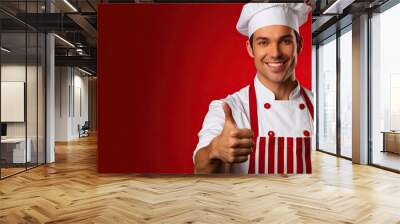 A confident and enthusiastic male chef wearing a striped apron white t shirt and chef s hat is standing against a red wall background He holds a check mark showing a thumbs up gesture This image repr Wall mural