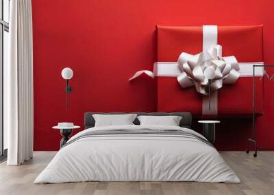 A festive Christmas gift box with a white bow on a red backdrop creating a seasonal ambiance in the copy space image Wall mural